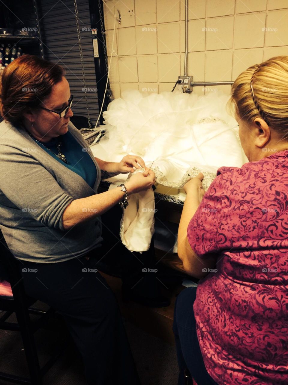 Two seamstresses hemming a bridal gown. Burning the midnight oil.