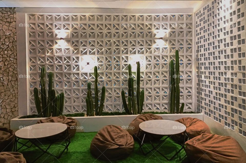 Modern minimalistic and bright living room in shades of dark white with bean bag chair, two coffee tables with carpet and cactuses on background and textured wall.