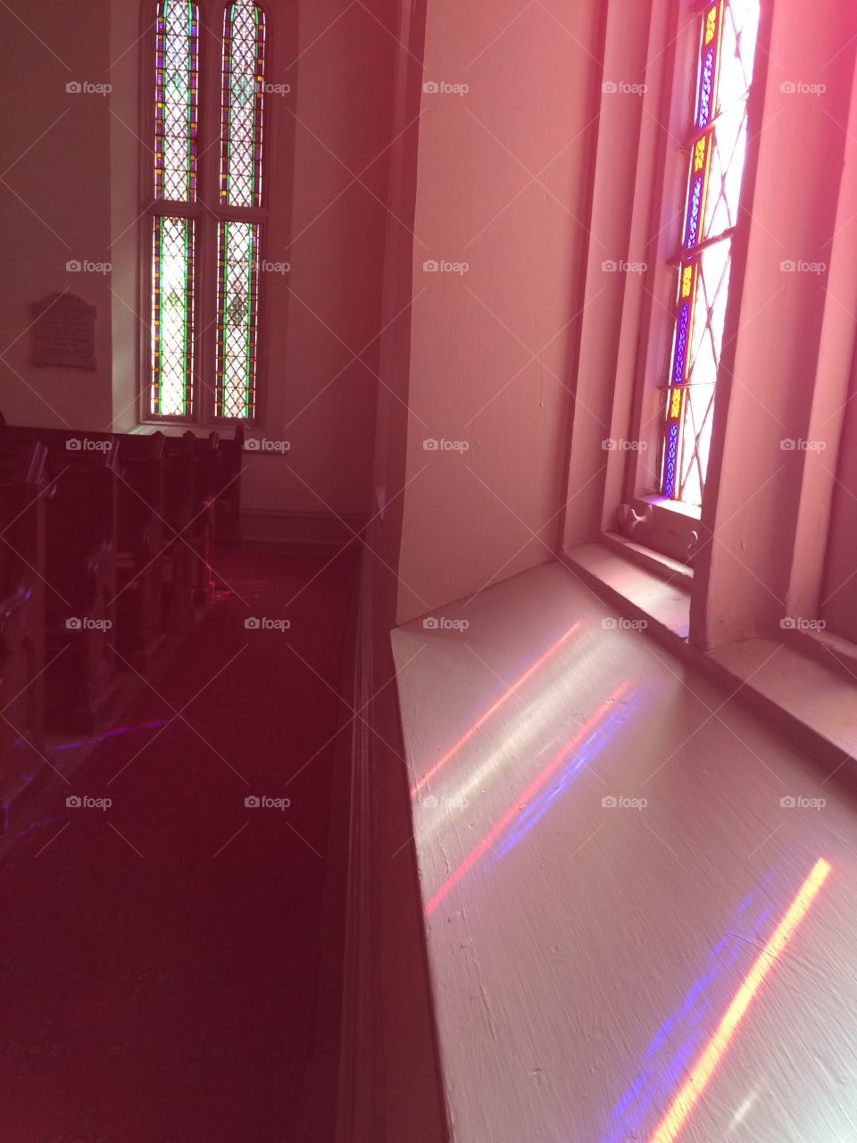 The beautiful stained glass window panes of an old church, the colorful light streaming in, covering the dusty carpets and antique pews with its warm glow. 