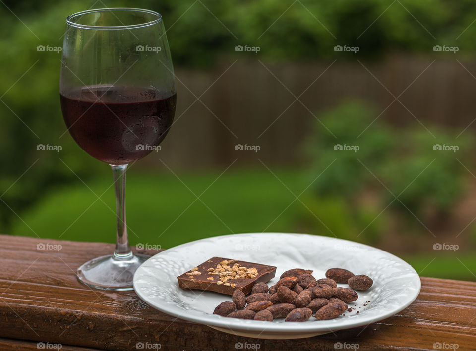 Chocolate with almonds, chocolate covered almonds on a white plate and red wine in a glass on a wet spring evening on the porch