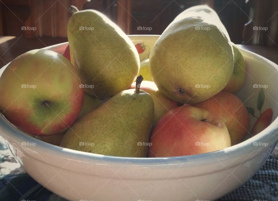 A bowl full of Gala Apples and green Pears close up in a kitchen in the morning light