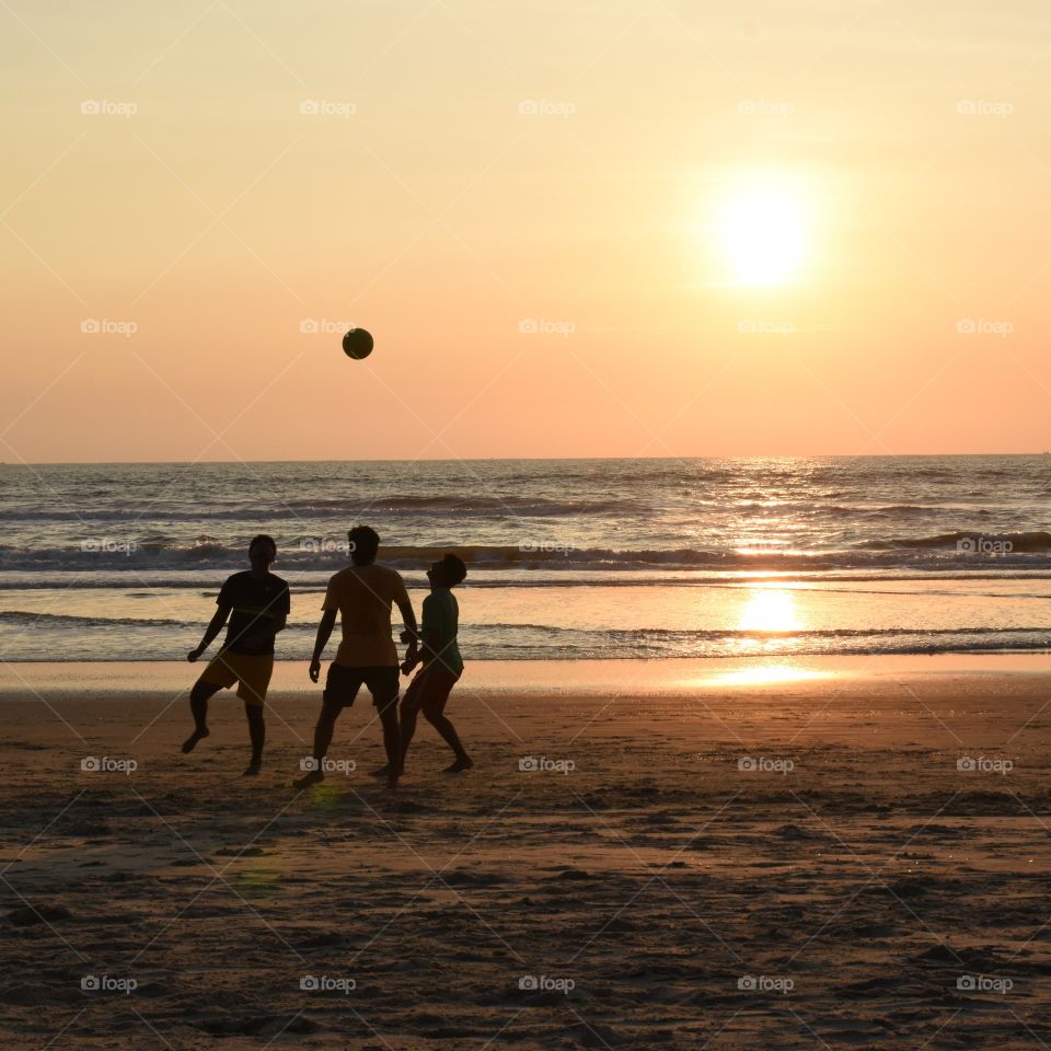 youngsters playing football on the beach during sunset....