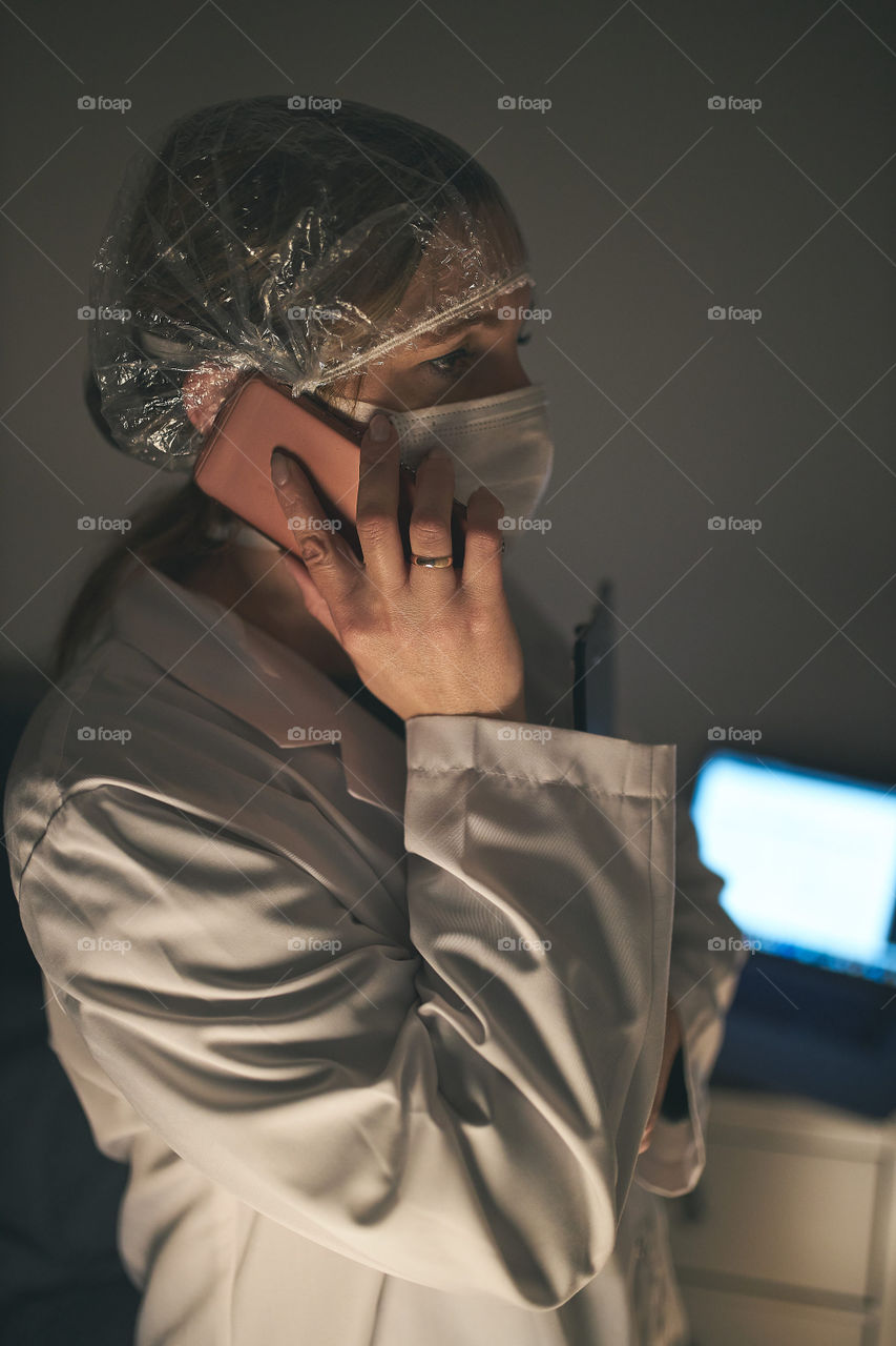 Doctor making a phone call. Hospital staff working at night duty. Woman wearing uniform, cap and face mask to prevent virus infection