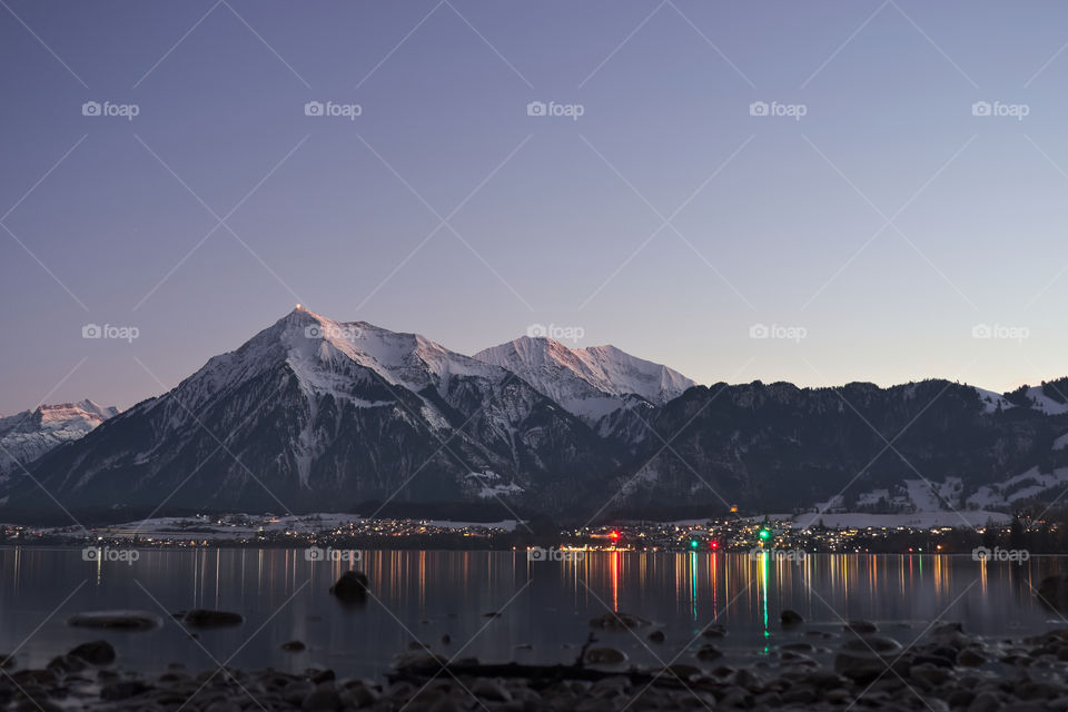 Mountain range (Niesen) with village lights reflecting in lake thun.