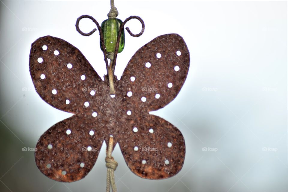 Garden ornament rusty butterfly against light sky background