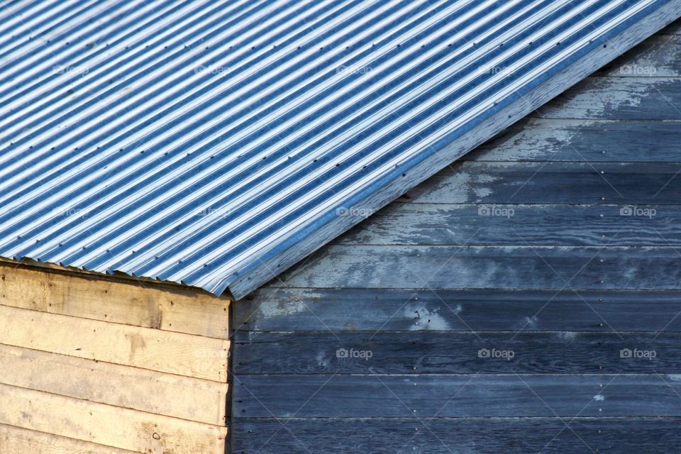 Outside corner of antique farm building with weathered wood, peeling paint, and a corrugated metal roof during golden hour 