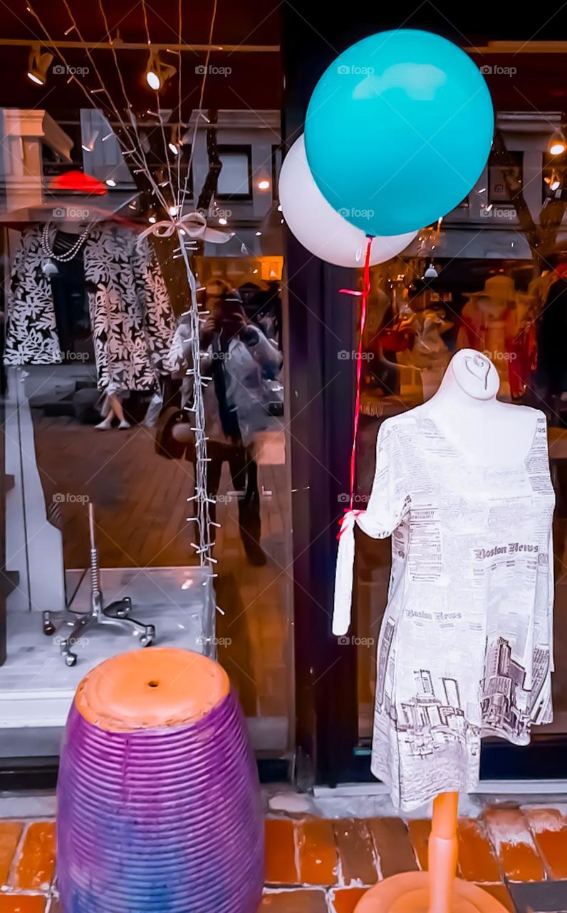 Shopkeeper, to draw attention, placed on the sidewalk in front of the store, a mannequin with two balloons tied to his arm and a huge purple vase.  In the background image of the photographer who is posting this image, reflected in the glass door.