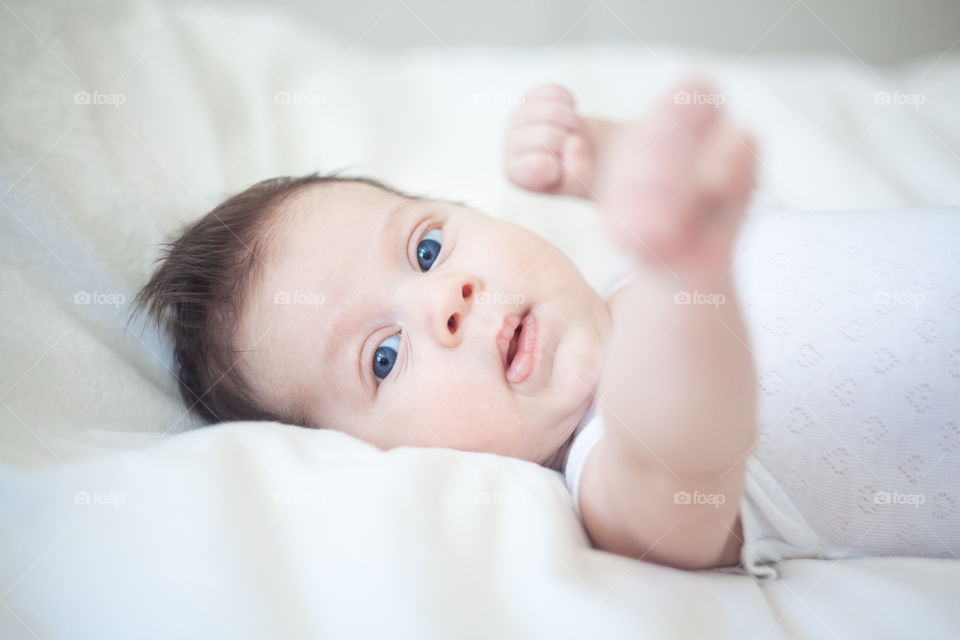 Infant baby with blue eyes laying on white bed background