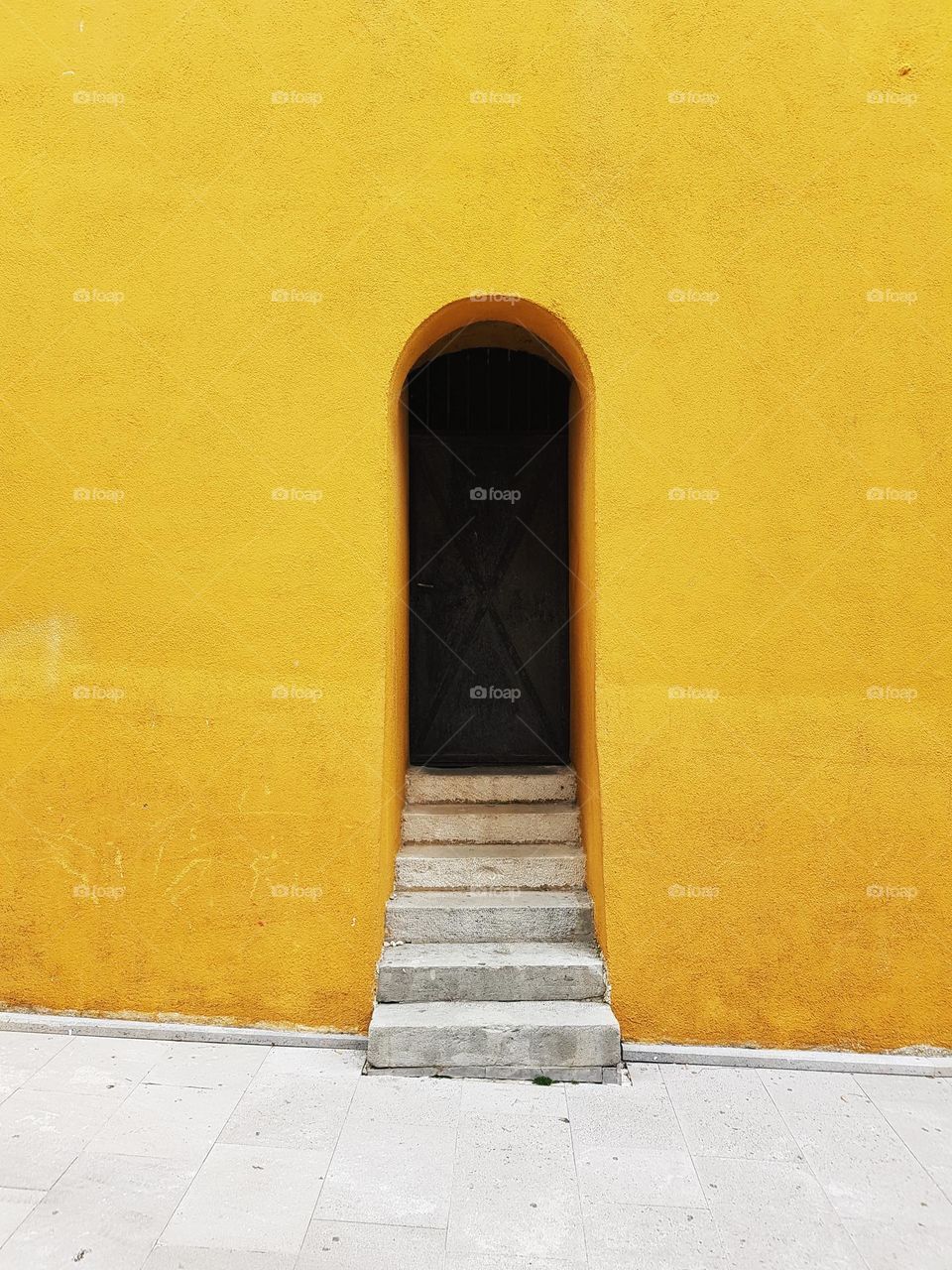 Stone steps leading to dark arched entrance on old building with yellow facade