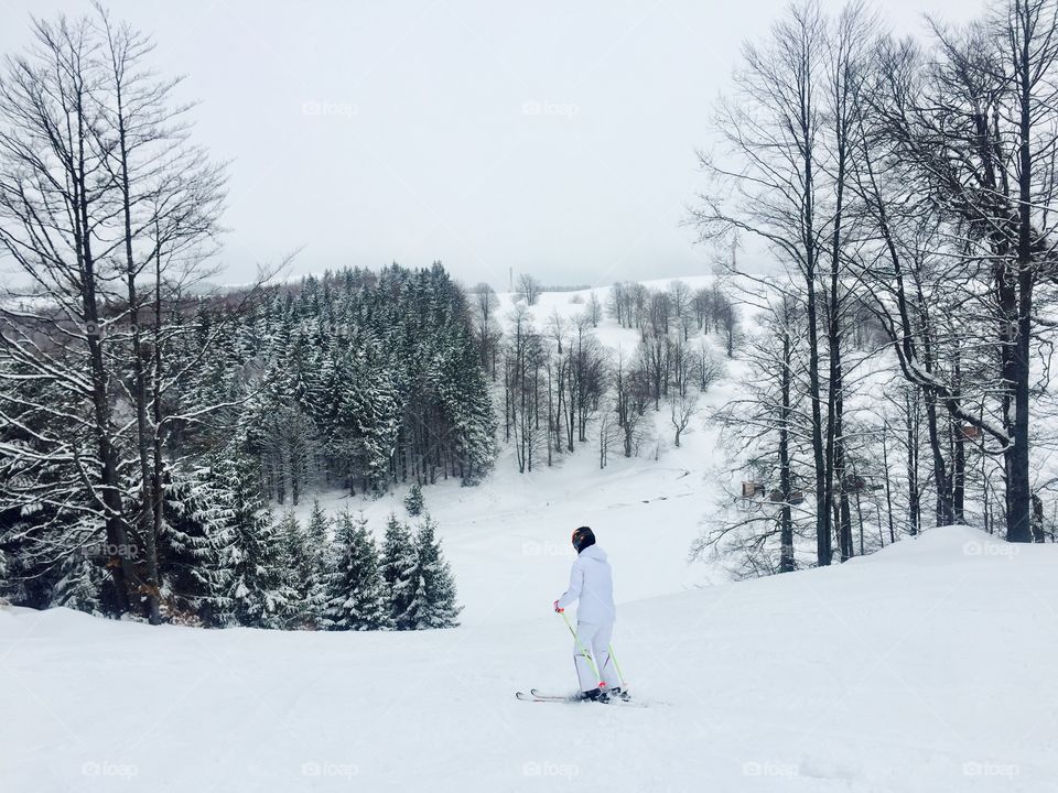 Woman in white ski costume on the ski slope surrounded by snowy forest