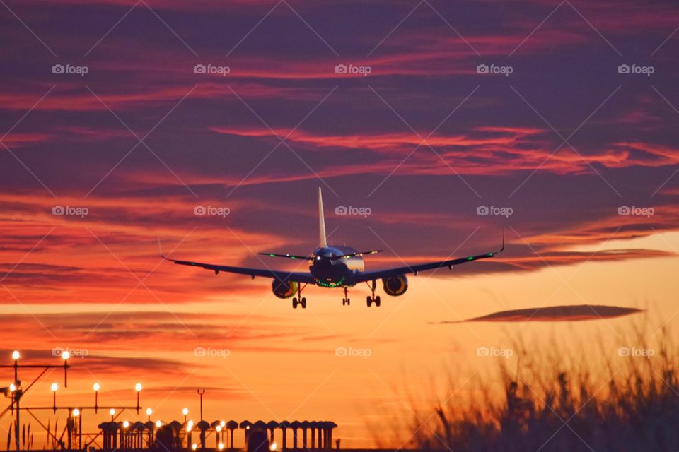 Plane landing during sunset against cloudy and orange sky