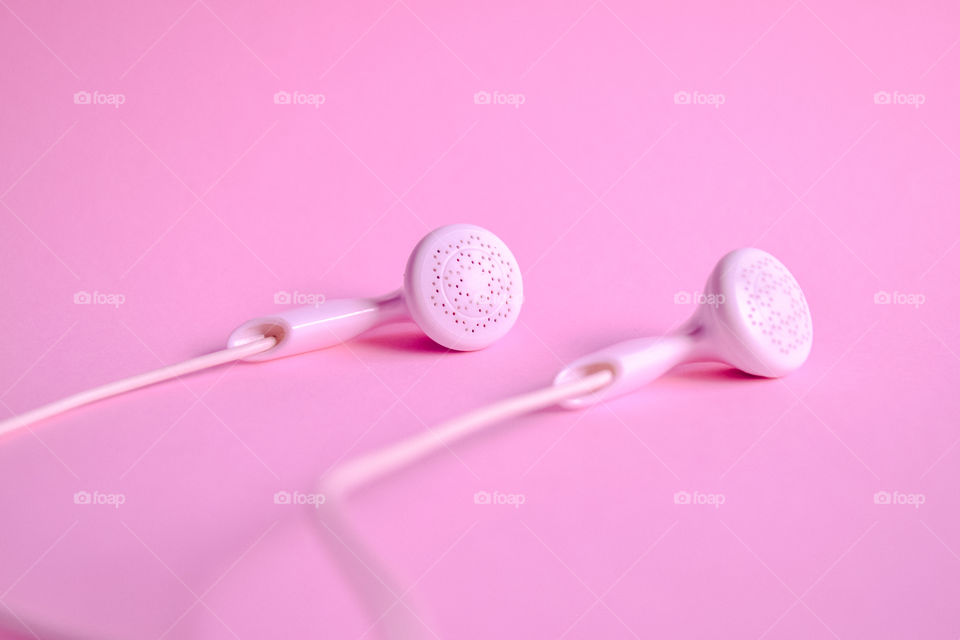 White in ear headphone on a pink background. Closed top view.