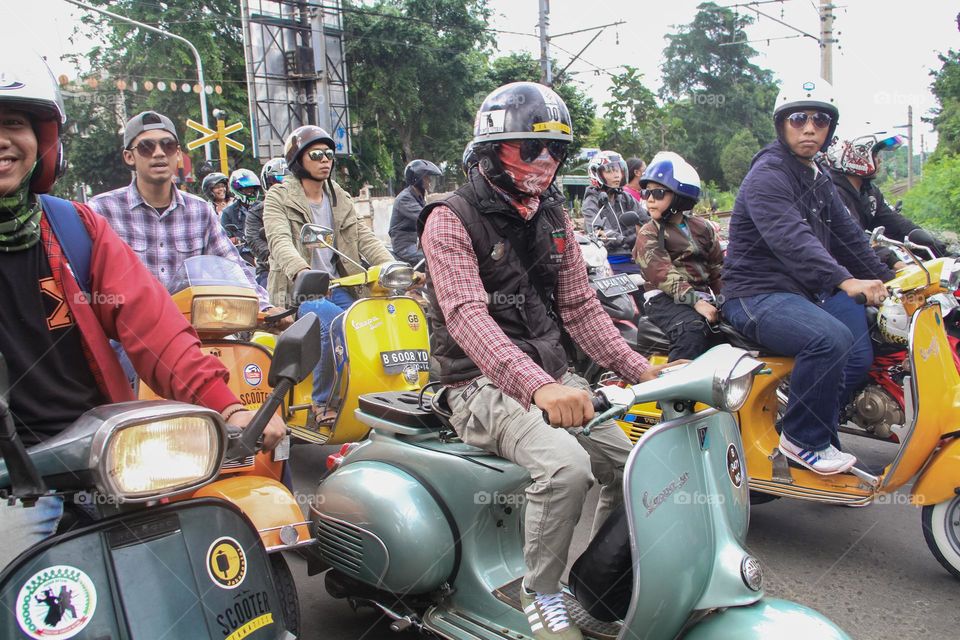 Portrait of a group of Vespa riders photographed from behind during a convoy on a street in Jakarta driving various types of classic Vespas.