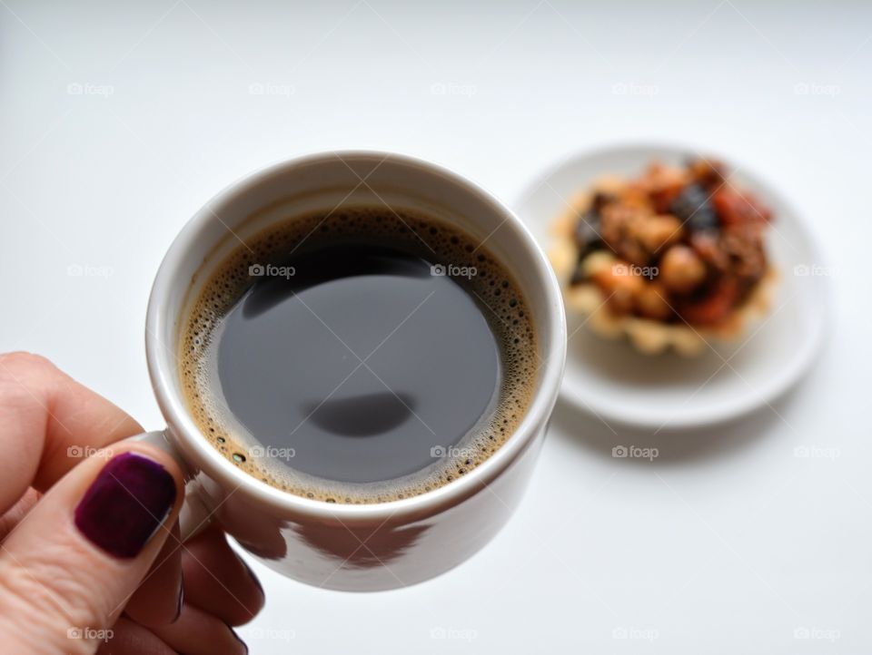 cup of coffee in the hand and cupcake on a plate on a white background, morning routine