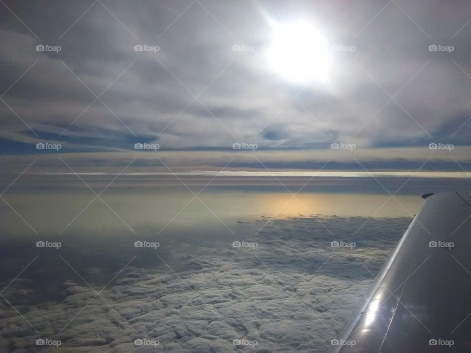 high altitude from plane above lake Michigan with sun reflecting on lake and bottom layer of clouds