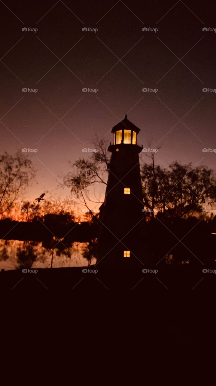 Lighthouse is gleaming that Night is near, backlit, mirrored image of lake reflections from the shore line mixed with backlit makes for a beautiful night.