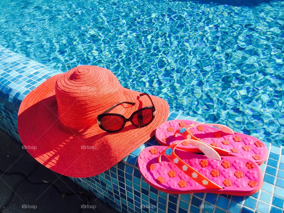 Red summer hat,pink flip flops and black sunglasses near the pool
