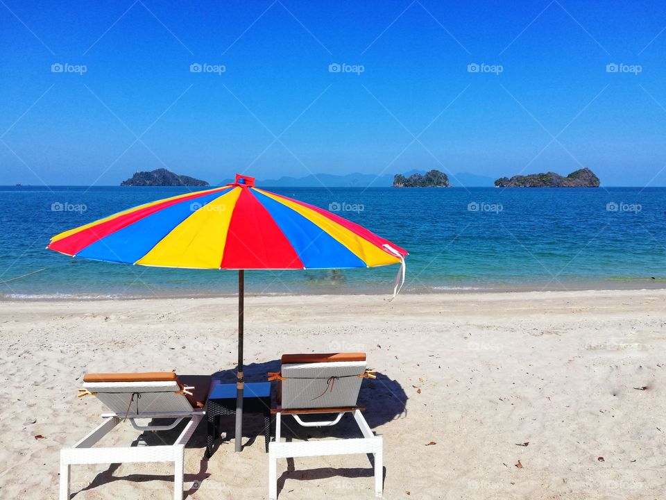 Colored beach umbrella and deck chair by the sea