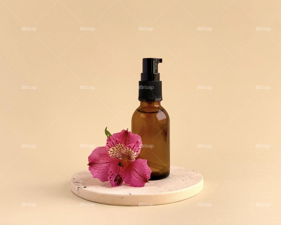 Glass bottle and pink flower on stone podium, cosmetic, care