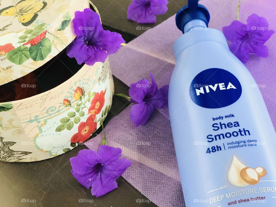 Nivea shea smooth body lotion with lavender flowers near a gift box .