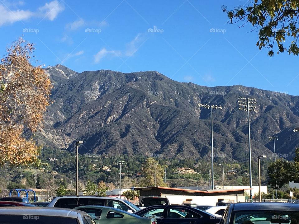 Sunny view of the mountains, with cars and a suburban setting in the foreground. 