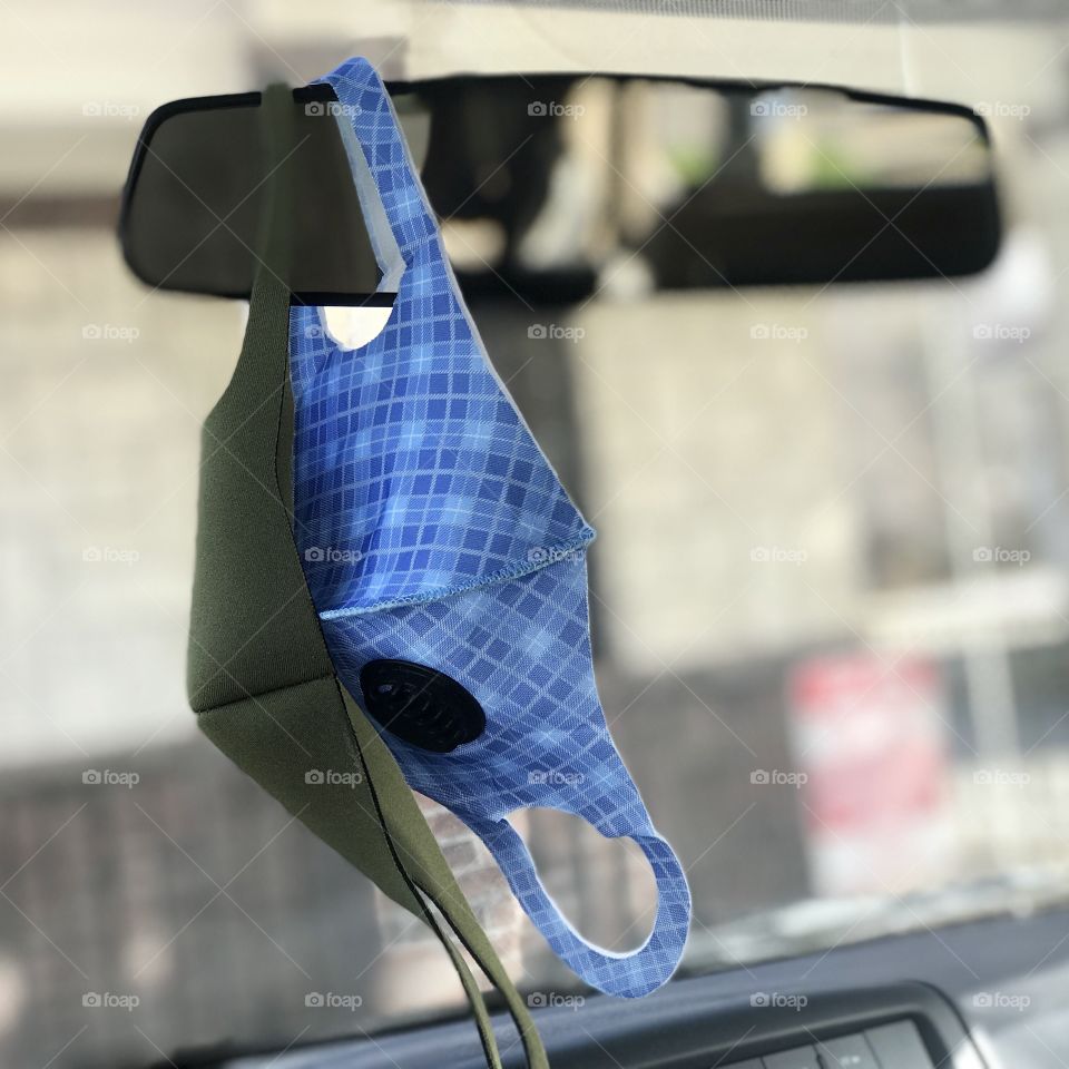 Two face masks hanging from a rear view mirror of a car.