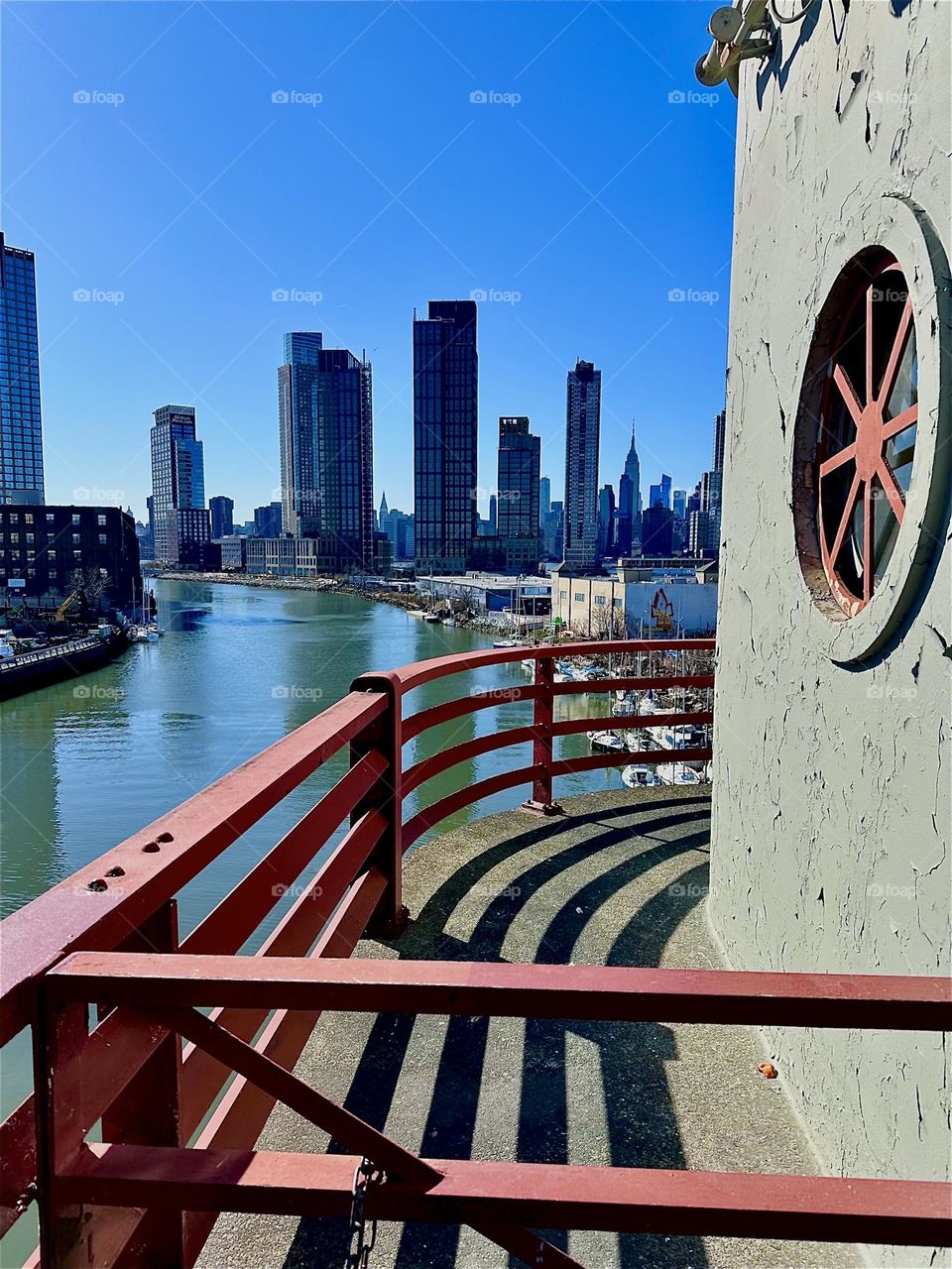 This is „Newtown Creek“ seen from the center outpost of the „Pulaski Bridge“ that connects LIC, Queens to „Greenpoint“, Brooklyn. In the far distance we can see the „Manhattan“ skyline including the „Empire State Building“. 2024. Hypnotic Productions