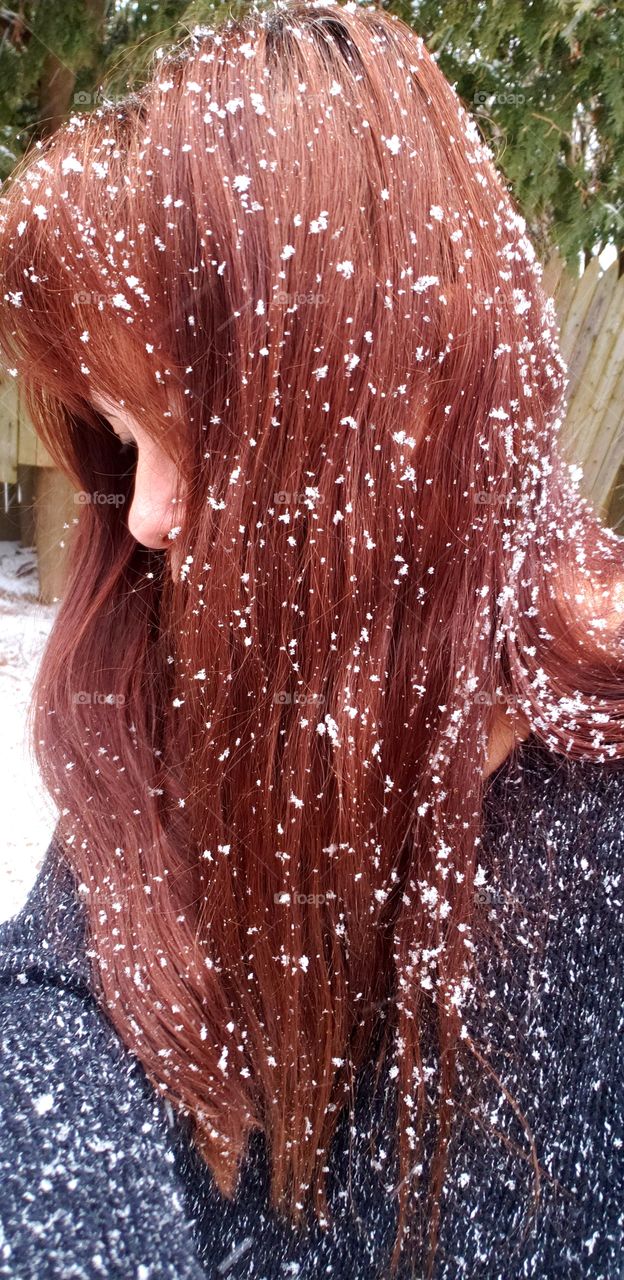 Unrecognizable woman with long red hair  that is sprinkled with large snowflakes