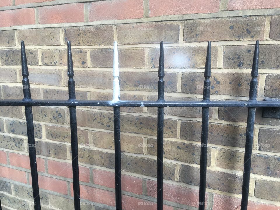 Metal spiked railings in front of a brick wall on Saint Thomas Street nr Guy’s Hospital, Southwark, London, passed in Summer. One white spike.