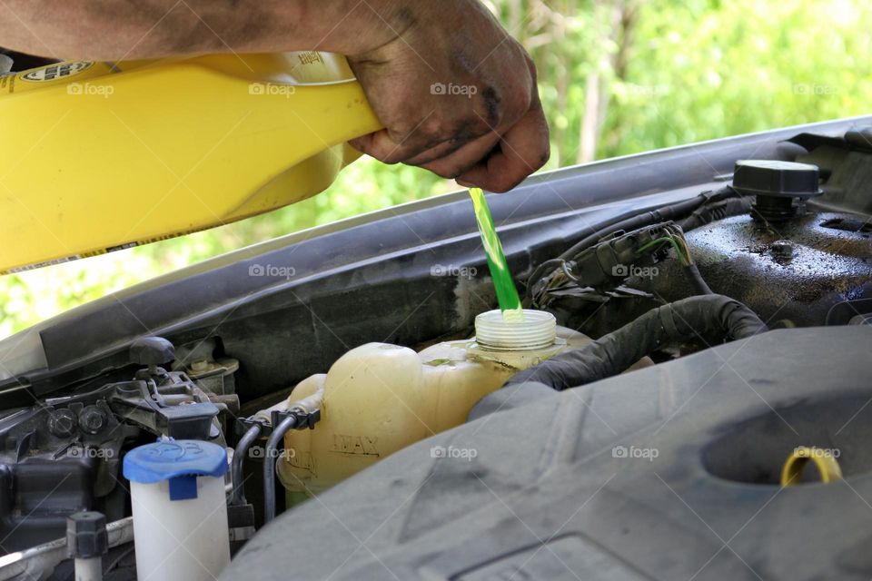 Car maintenance (checking fluids): a man is topping up his coolant at home.