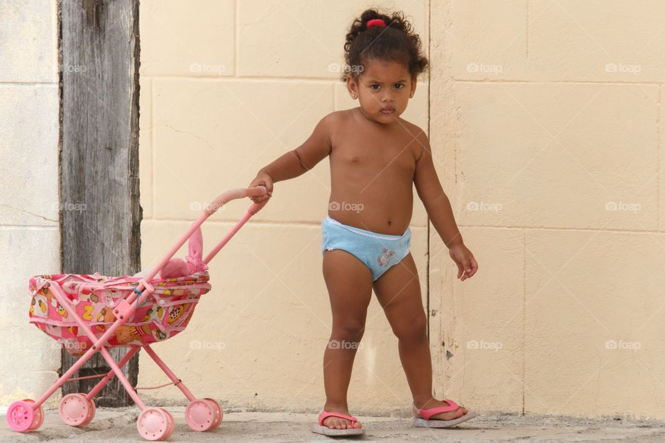 Cuban People.Cute little girl playing with her toy carriage outdoors.