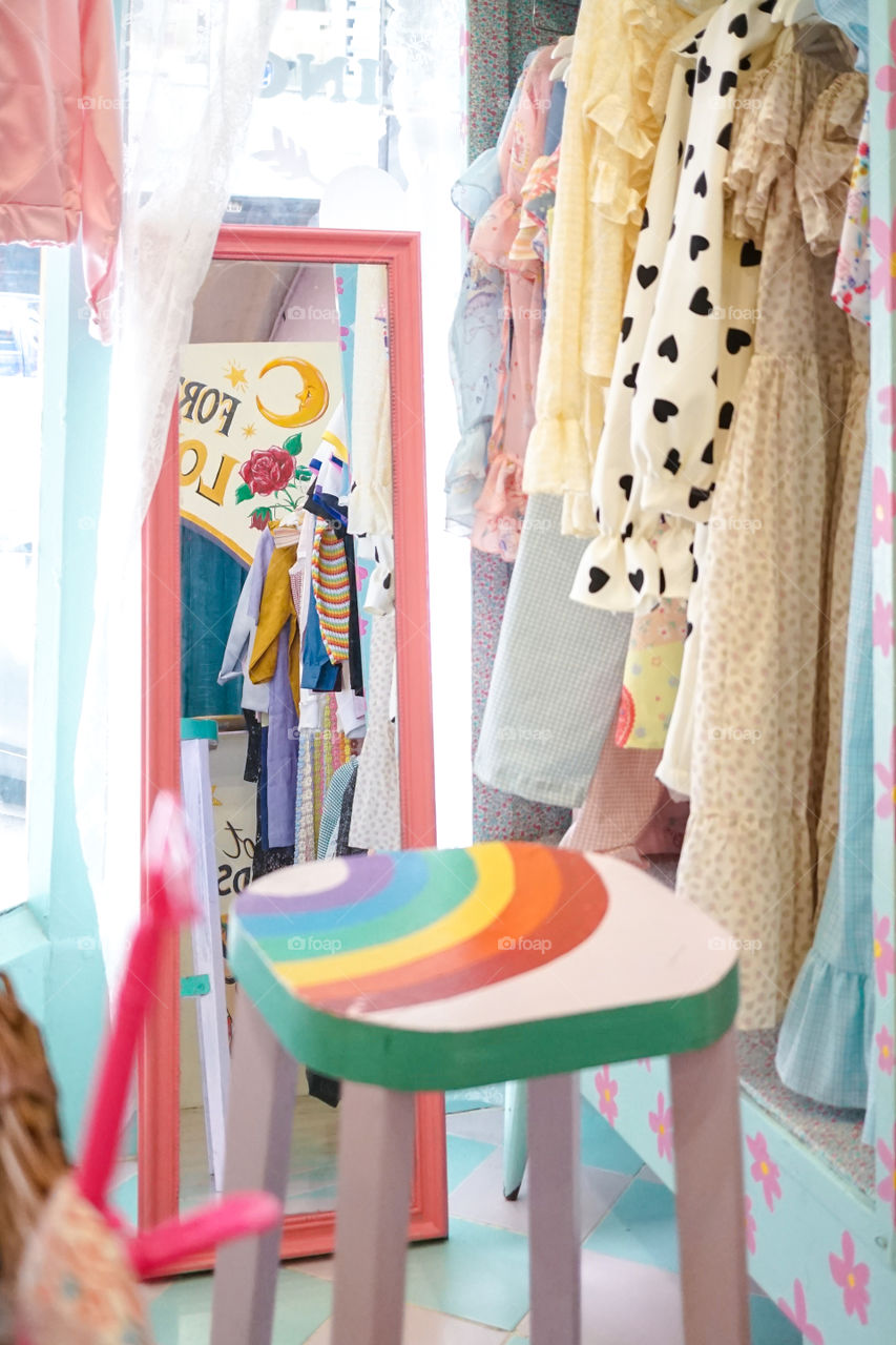 A photo of lady cloth shop interior. Inside of a lady cloth shop with abstract blur of wooden stool as foreground and selective focus on the mirror. Bangkok, Thailand