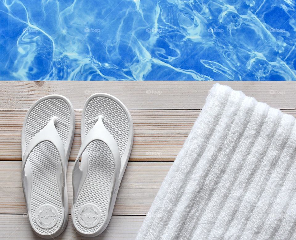 White flip flops poolside with a white towel 