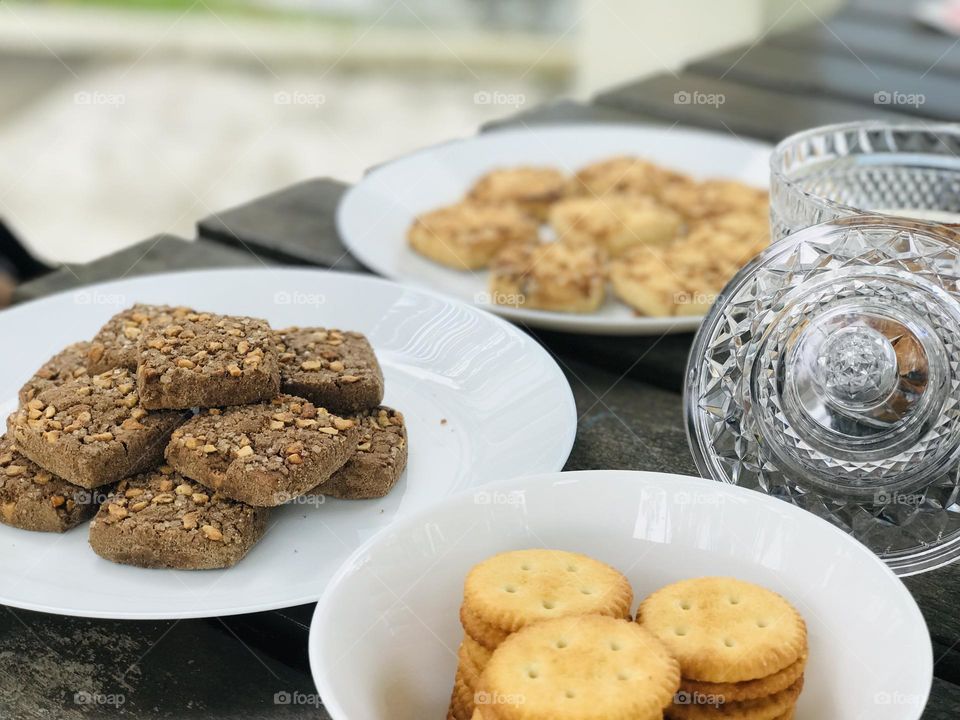 A plate full of brown and white cookies voted with dry fruits (nuts)and also a bowl full of salted cookies arranged on table 