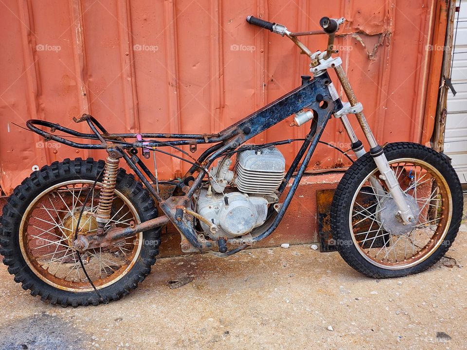 An old motorcycle sits decaying alongside a building and missing many critical parts