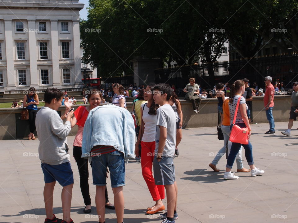 A group of young people standing in a circle talking and laughing together on a sunny summer day in London. 