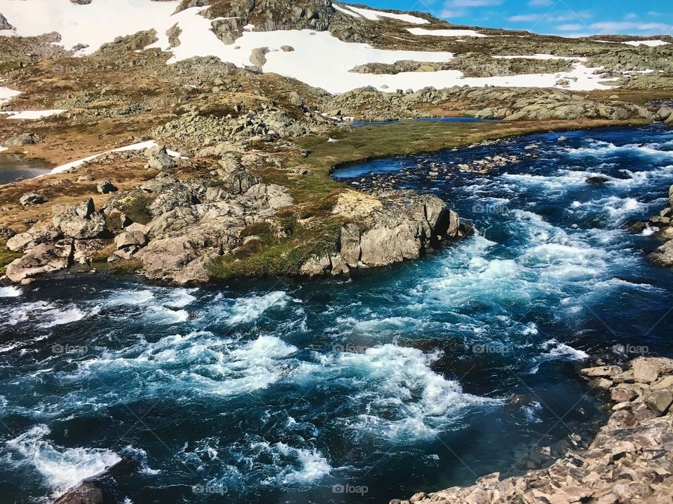 Slow moving stream with snow covered mountains in Norwegian fjords