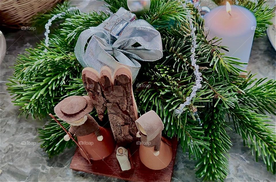 These miniature “Nativity” Christmas figures presented in “Bavaria”, Germany with a bow, a small silver gift box, evergreen twigs and a white candle are vintage items handcrafted from wood, fabric and leather. 2023. Hypnotic Productions