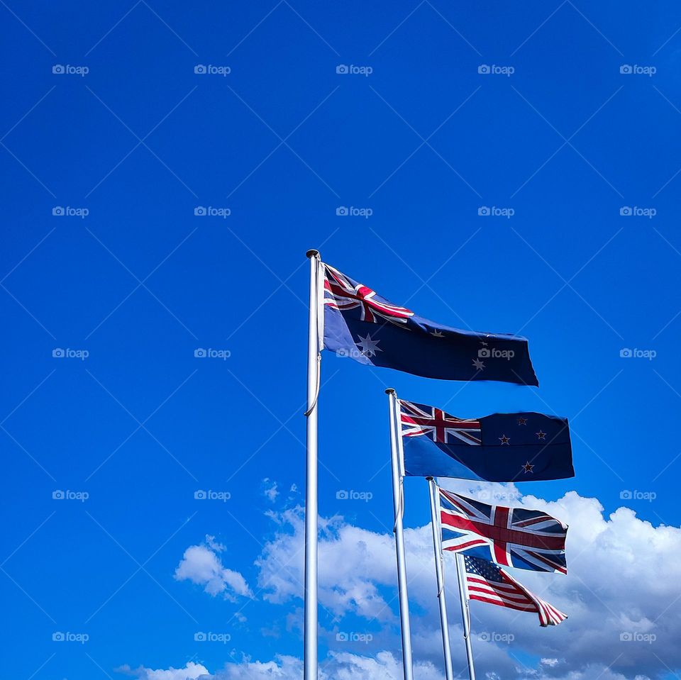 Australian, New Zealand, United Kingdom and USA flags blowing in the wind against blue sky.