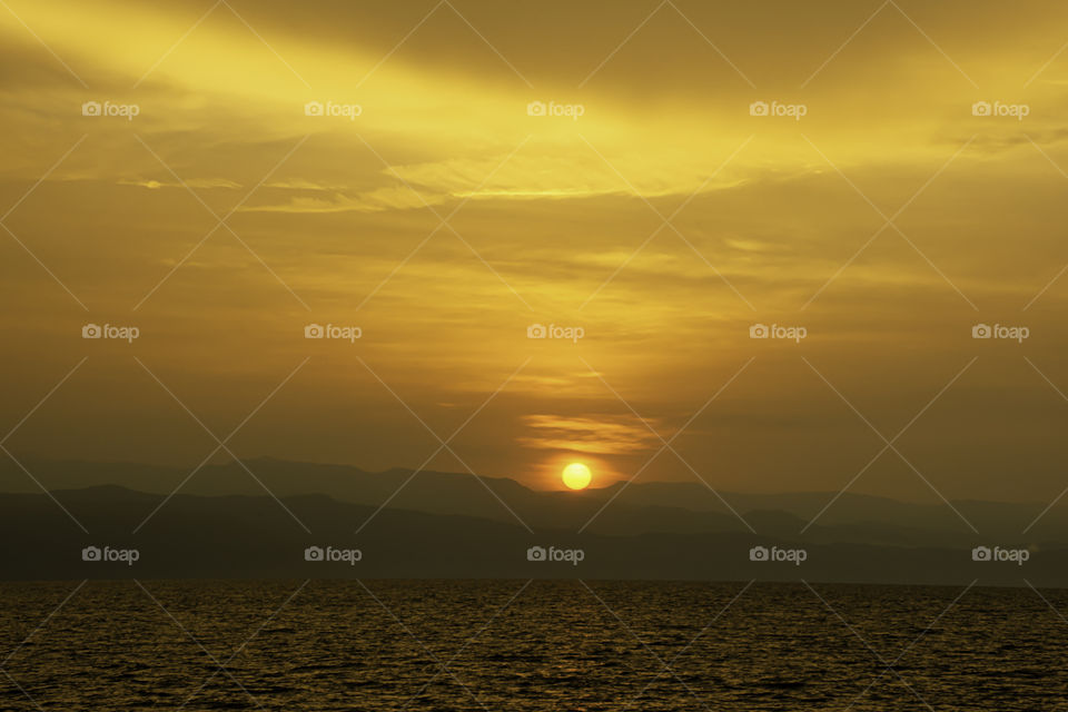 Golden light of sunrise behind the mountains and the sea.