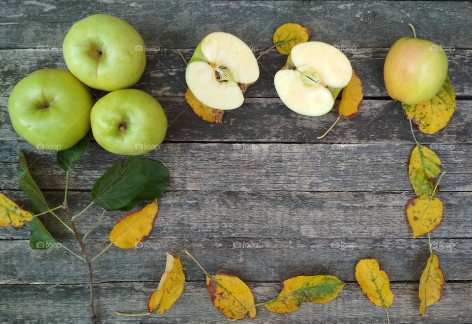 Autumn wallpaper with green apples and yellow leaves on wooden background.