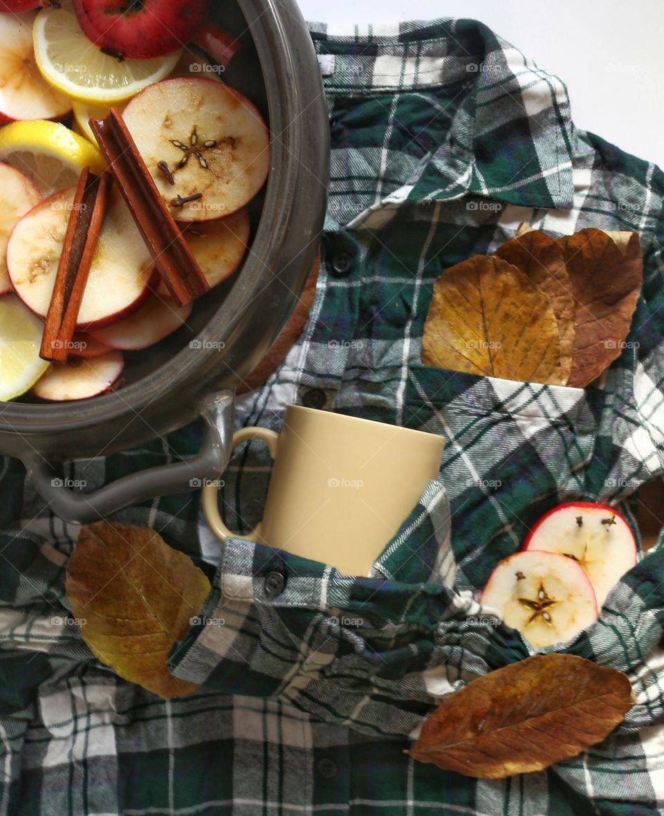 Flatlay of a Crockpot of brewing apple cider alongside fall leaves and apple slices.