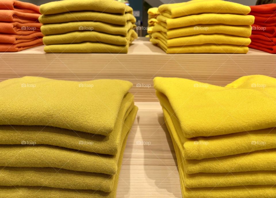 stack of folded yellow sweaters displayed on the wooden shelves of a clothing store