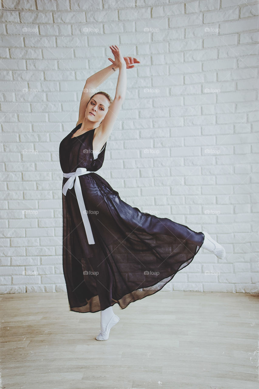 Young and graceful ballerina in pointe shoes and a dark dress dances in a studio. Choreography and dancing classes concept. Creative ideas of ballet posing and performance.