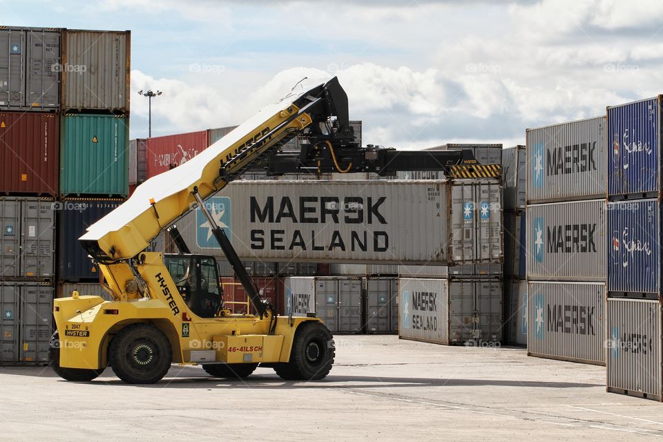 A heavy machine lifter transporting a shipping container around a yard and stacking them up high.