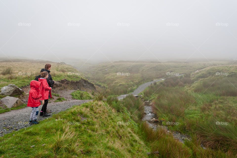 Family on outdoors walk in moorlands approaching stream.