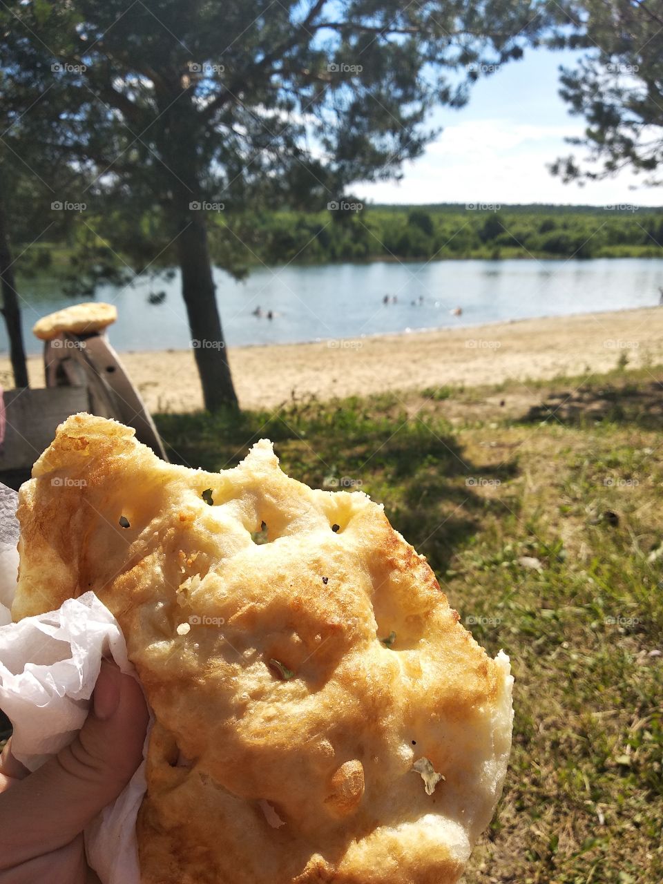 Fried flatbread, cake in hand against the background of the beach, lake and tree