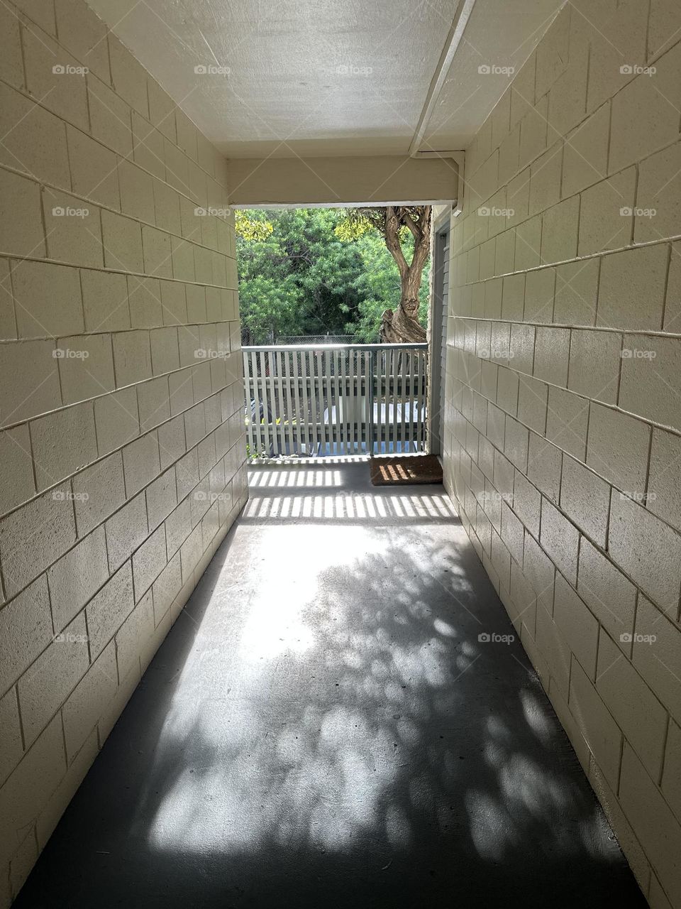 Cinder block hallway in 1962 condo with off white semi gloss paint and matte grey painted concrete floor leading to blue grey painted wood picket fence railing