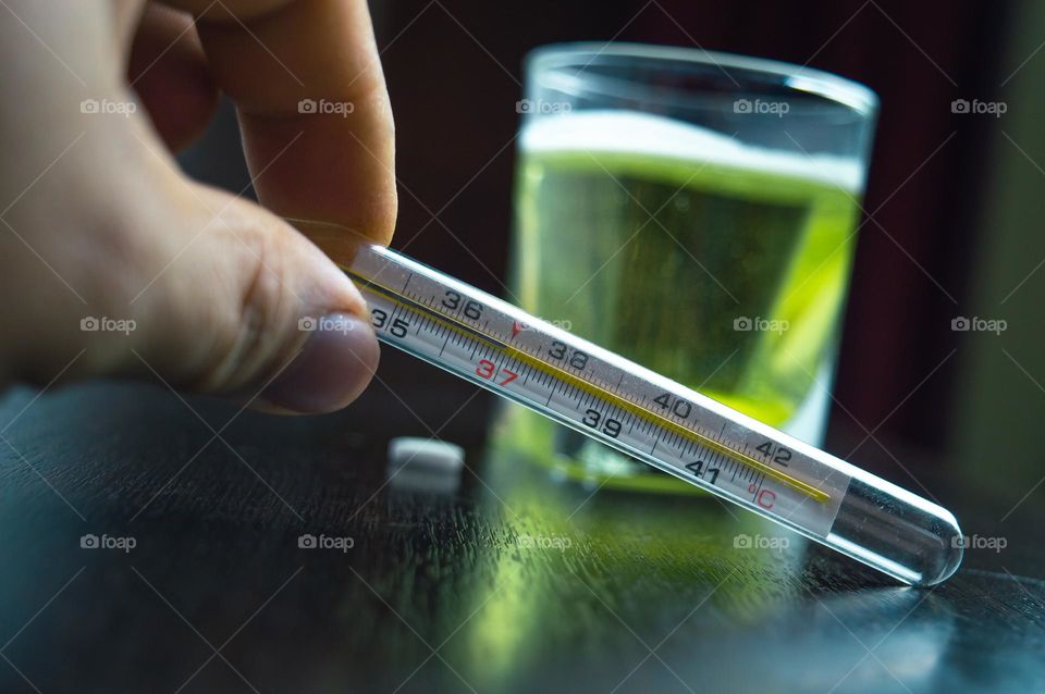 New Year's flu with a little vitamin C and a thermometer in the foreground. behind there is a glass with medicine and a pill next to it