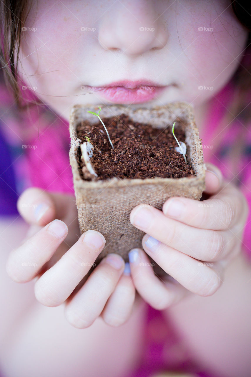 Girl holding flower pot with new seedling growing in her hands. New leaves.